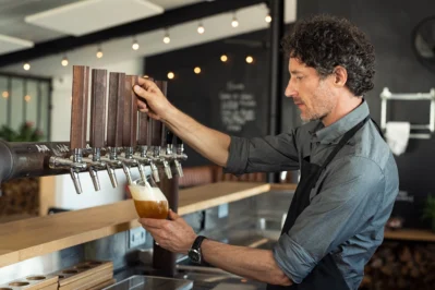 Empreendedor em seu bar, servindo uma cerveja, representando a implementação do Imposto do Pecado, também conhecido como Imposto Seletivo