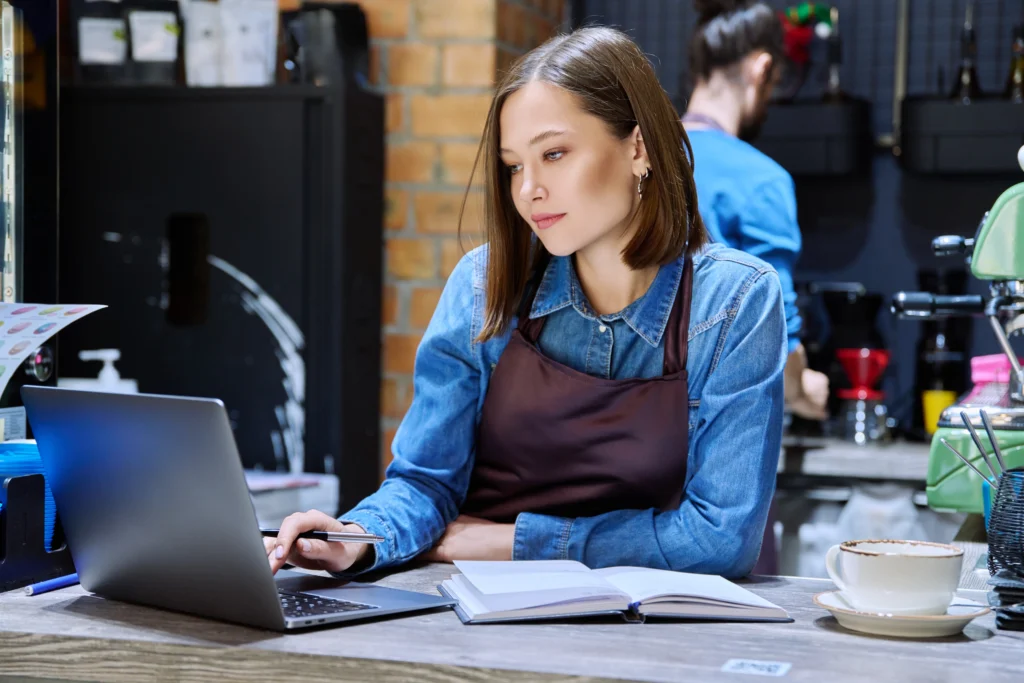 Empresária em seu negócio, mexendo no computador. Ela está entendendo as mudanças da reforma tributária no Simples Nacional.